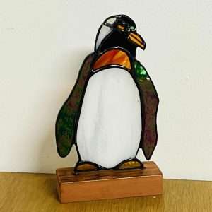 Stained glass penguin ornament on a wooden base.